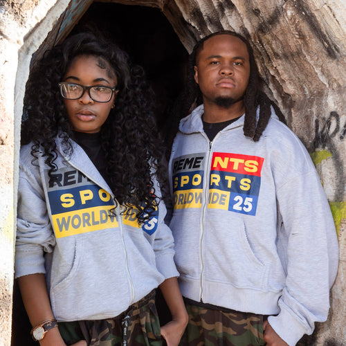 Two models wearing matching light gray zip-up hoodies with a colorful 'Ceme Sports Worldwide 25' graphic, paired with camouflage pants, standing in front of a stone doorway.